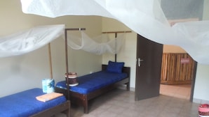 Une chambre avec deux lits simples, une porte en bois et un sol carrelé.