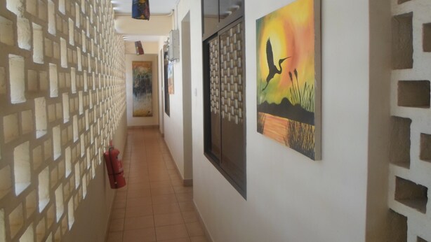 Un couloir avec un mur orné de motifs, un tableau représentant un oiseau et un sol carrelé.