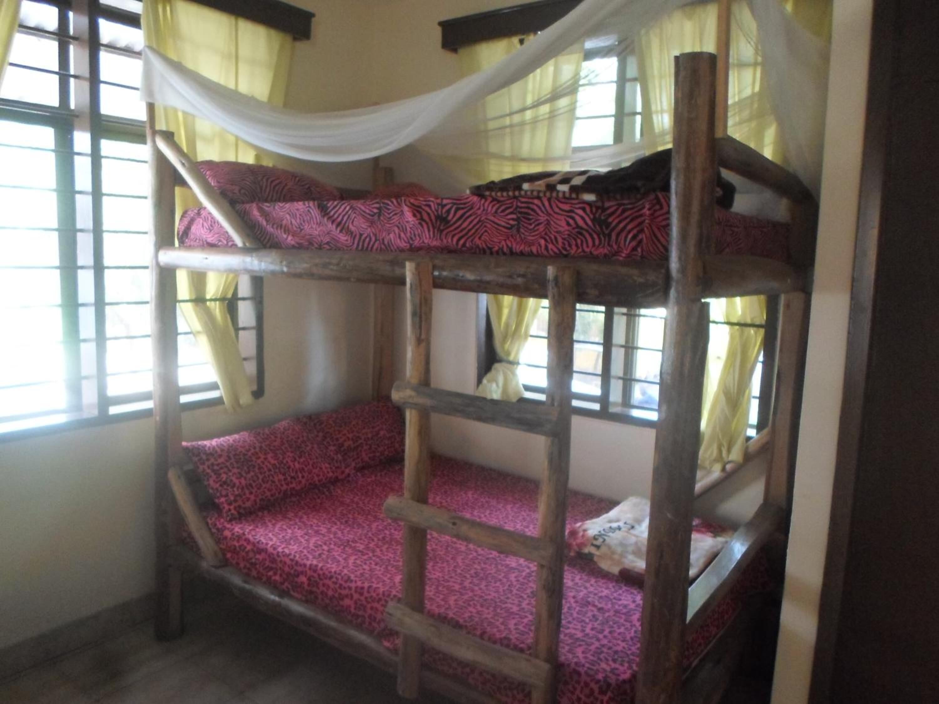 A bunk bed with a ladder, a window with yellow curtains, and a wooden headboard.