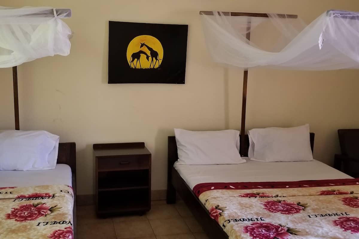 A room with two beds, each with a canopy. There is a nightstand between the beds, and a framed picture on the wall.