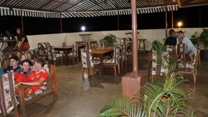 Un espace extérieur aménagé pour les repas, avec des tables et des chaises, un toit en métal et des plantes en pot.