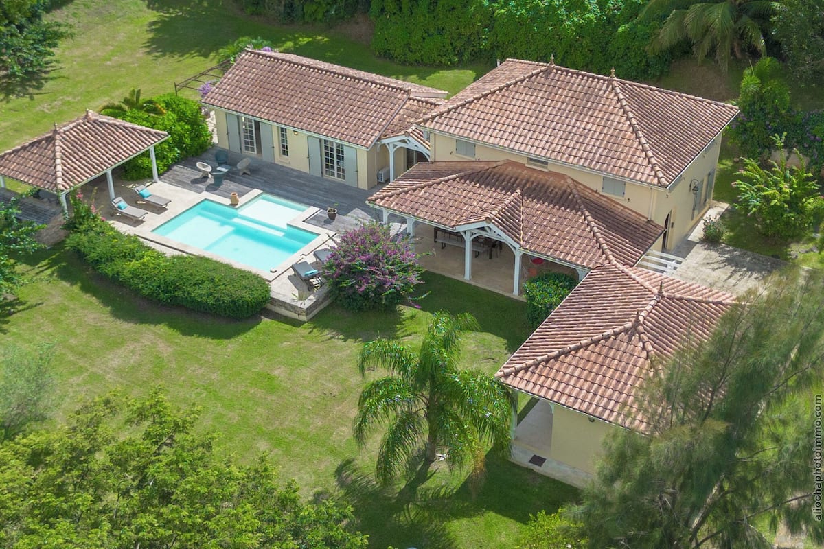 An aerial view of a house with a swimming pool, multiple patios, and a well-maintained lawn.