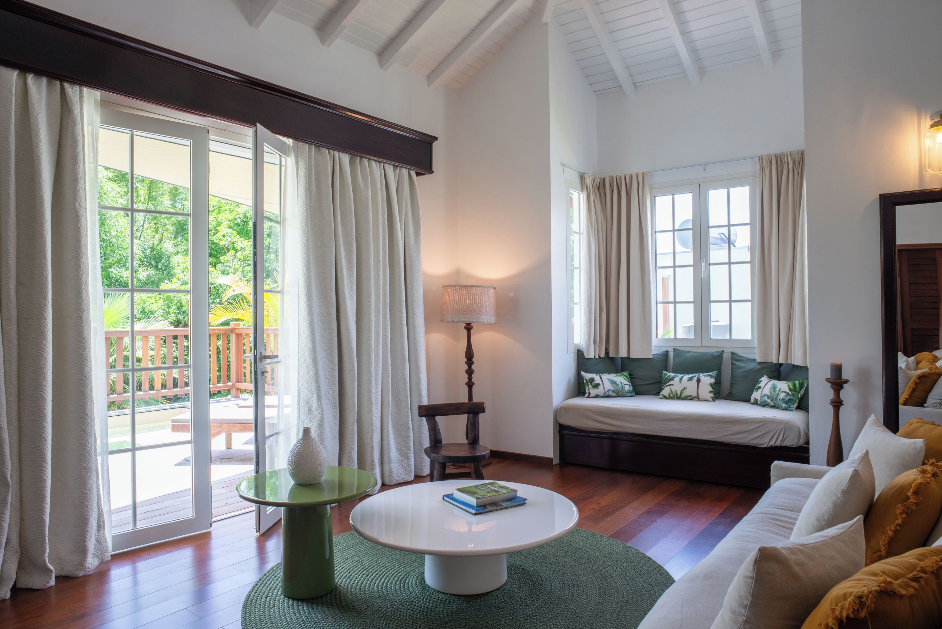 A room with a large sliding glass door, a round table with a book, a sofa with cushions, and a lamp.