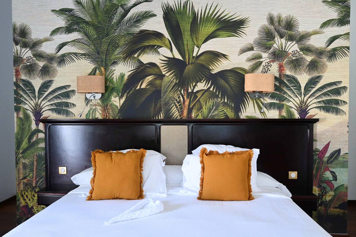 A hotel room with a large bed, two wall-mounted lamps, and a tropical-themed mural on the wall.