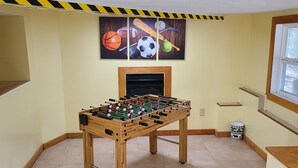 A room with a wooden foosball table, a fireplace, and sports-themed wall art. - Cozy Cottage - Located on App Ski Mtn Lower level game room, Firepit (Blowing Rock)