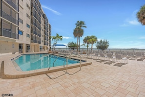 A swimming pool with lounge chairs and palm trees, surrounded by a building with balconies. - Gulf Front 2B/2B Vacation Condo At Carlos Pointe Beach Club With Amazing Views! (Fort Myers Beach)