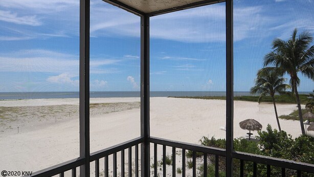 Vista de la playa desde un espacio cubierto con barandilla, palmeras y cielo despejado.