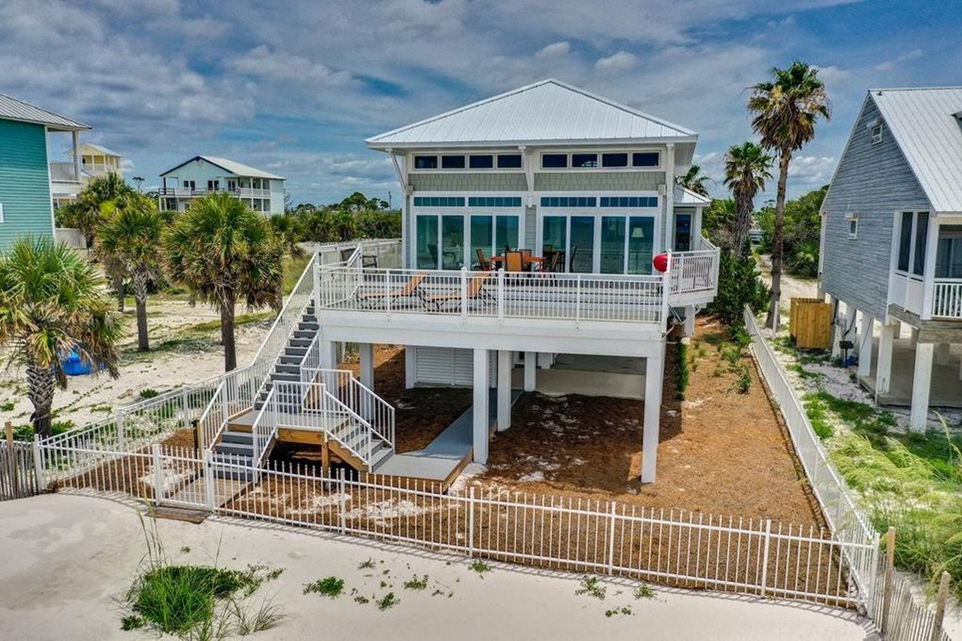 Una casa frente a la playa con un porche cubierto y una escalera que lleva al segundo piso.