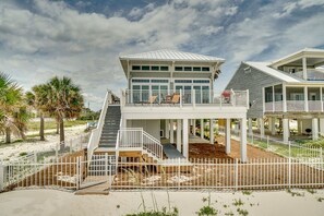 A beachfront property with a main house and a guest house, featuring a covered deck and a staircase leading to the main house.