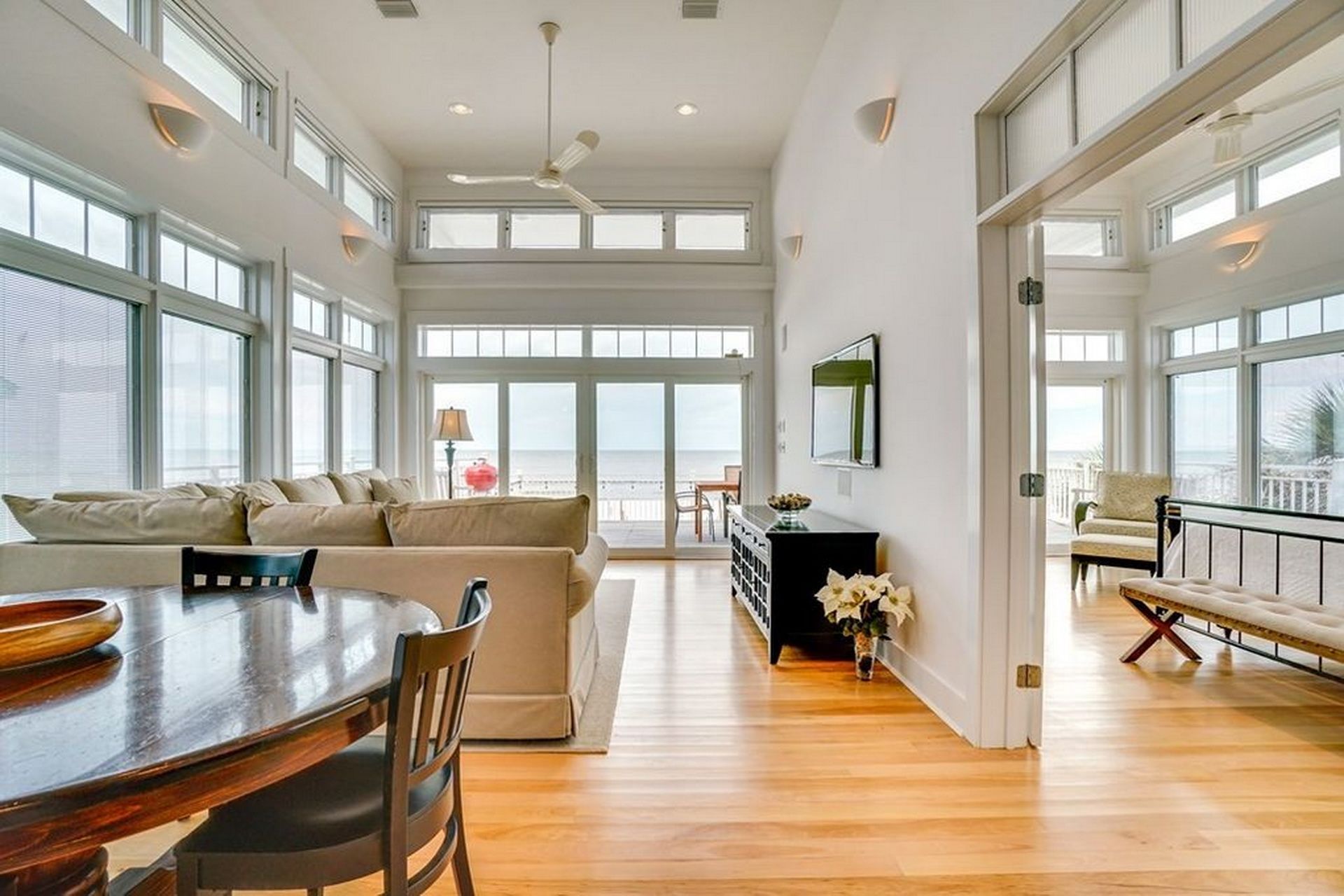 A spacious living area with a wooden dining table, a sofa, and a view of the ocean through large windows.