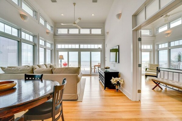 A spacious living area with a wooden dining table, a sofa, and a view of the ocean through large windows.