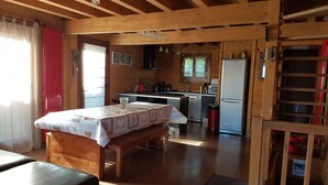 A cozy wooden interior with a dining table, bench, and kitchen area including a refrigerator and sink. - SLOPESIDE CHALET (DOUCY VALMOREL)
