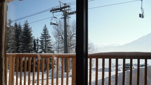 A view from a balcony with a wooden railing, overlooking a snowy landscape with trees and a ski lift. - SLOPESIDE CHALET (DOUCY VALMOREL)