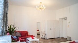 A living room with a red sofa, white coffee table, and a chandelier. There is a white wardrobe and a small plant on the left.
