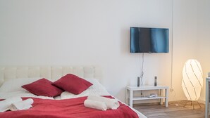 Ein Hotelzimmer mit Bett, Wandfernseher, Nachttisch mit Lampe und Stuhl.