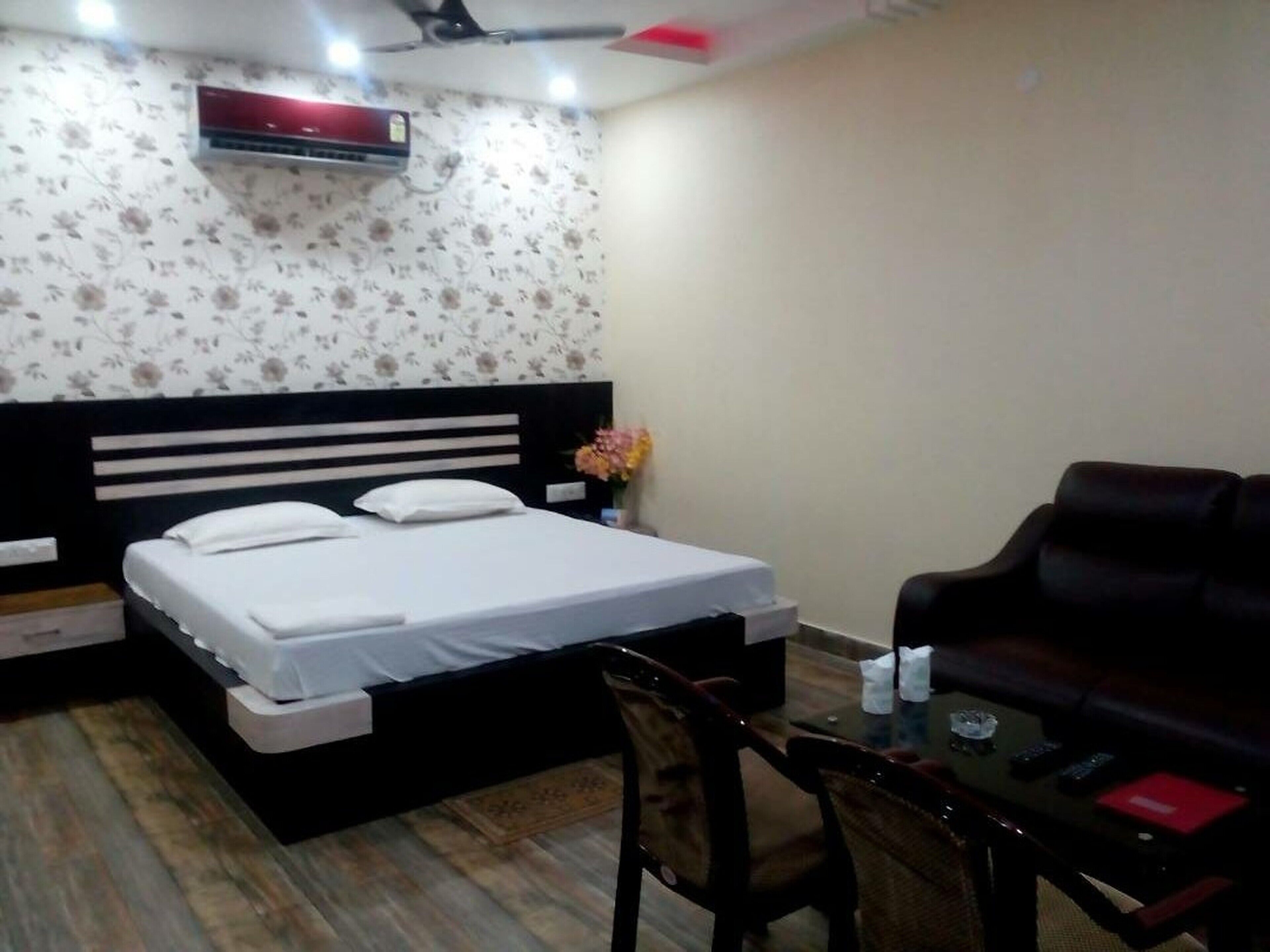A hotel room with a bed, a desk, a chair, a table, and an air conditioning unit.