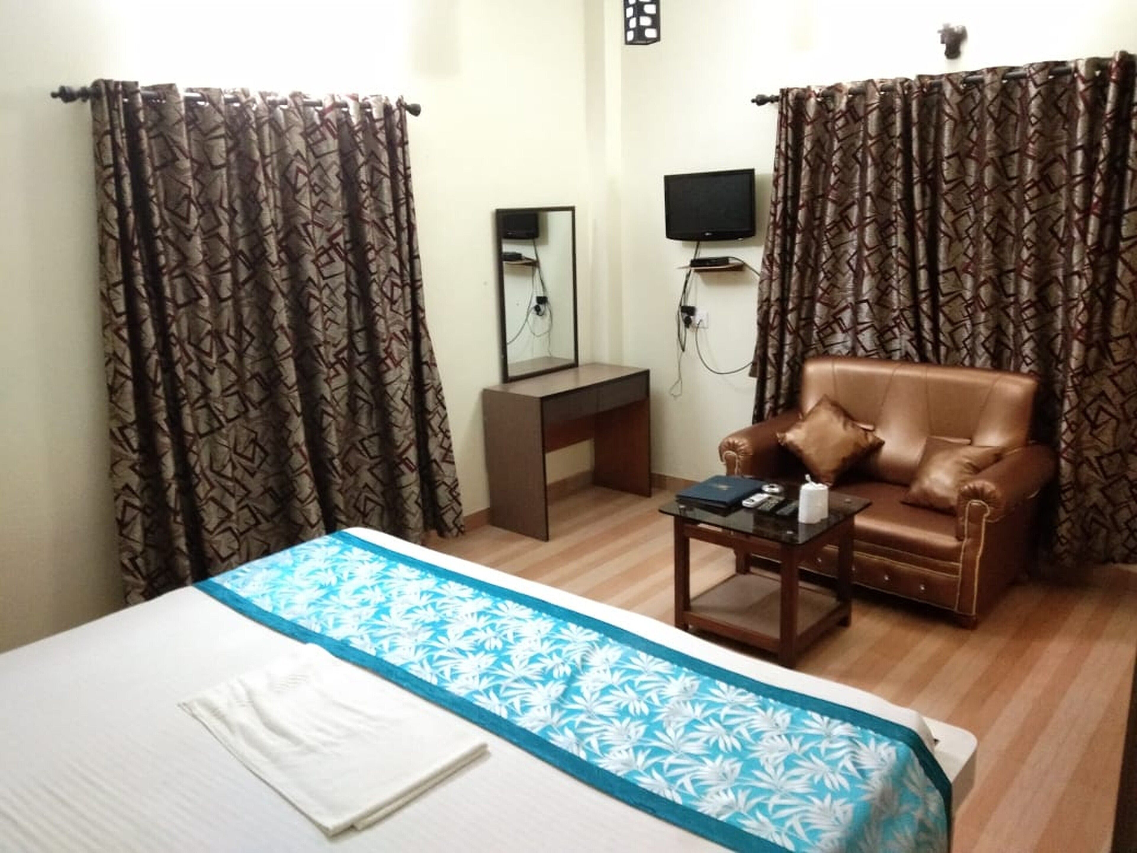 A hotel room with a bed, a sofa, a small table, a TV, and curtains.