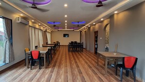 A spacious room with a long table and chairs, air conditioning units, ceiling fans, and large windows with curtains. - Mohana  Beach Resort (Kanthi)