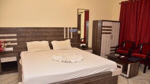 A neatly made bed with a white duvet, a bedside table with a lamp, and a mirror. There is a wooden wardrobe and a red curtain in the room. - Mohana  Beach Resort (Kanthi)