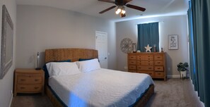 A bedroom with a bed, a dresser, a nightstand, a ceiling fan, and a wall with a decorative piece. - Pet Friendly Lodging Close to Whiteman AFB and Warrensburg (Warrensburg)