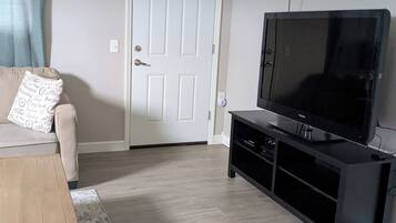 Una sala de estar con un sofá, una mesa de centro, un televisor en un mueble y una puerta.