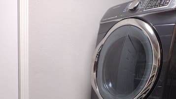 Une machine à laver et un sèche-linge superposés dans une buanderie, avec une porte blanche et un sol carrelé.