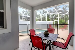A modern room with a glass balcony, a pool, and red chairs around a table with a decorative bowl.