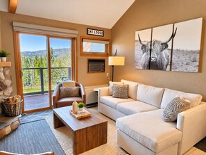 A modern living room with a sofa, armchair, coffee table, and a view of the outdoors through a sliding glass door. - Ski-In/Ski-Out 1BR+Loft | Moose Mtn Views | Pool (Lutsen)