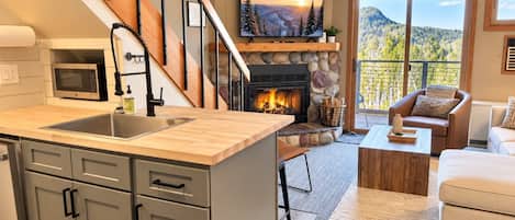 Een moderne keuken met een stenen openhaard, een eethoek met uitzicht en een trap naar een balkon.