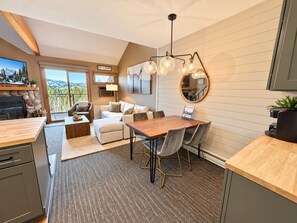A modern kitchen with a dining area, a fireplace, and a view of the mountains. - Ski-In/Ski-Out 1BR+Loft | Moose Mtn Views | Pool (Lutsen)