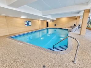 An indoor swimming pool with a tiled floor, a pool ladder, and a wall-mounted information board.