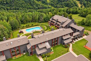A modern building with a swimming pool, surrounded by a well-maintained lawn and forested hills. - Ski-In/Ski-Out 1BR+Loft | Moose Mtn Views | Pool (Lutsen)