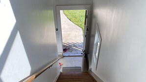 Una escalera de madera que lleva a una puerta con vista a un espacio verde exterior.