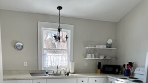 Una cocina con gabinetes blancos, un tapete estampado, una lámpara de araña y un microondas.