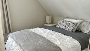 Un dormitorio con una colcha blanca con volantes, una manta gris y almohadas estampadas.