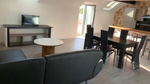 A modern living space with a sofa, a dining table with chairs, a TV on a stand, and a kitchen area with a refrigerator and cabinets. - Le domaine de frehel (Frehel)