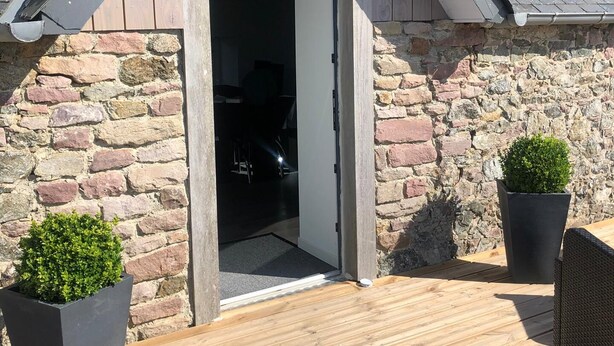 A stone building with a wooden deck, a door leading inside, and two potted plants. - Le domaine de frehel (Frehel)
