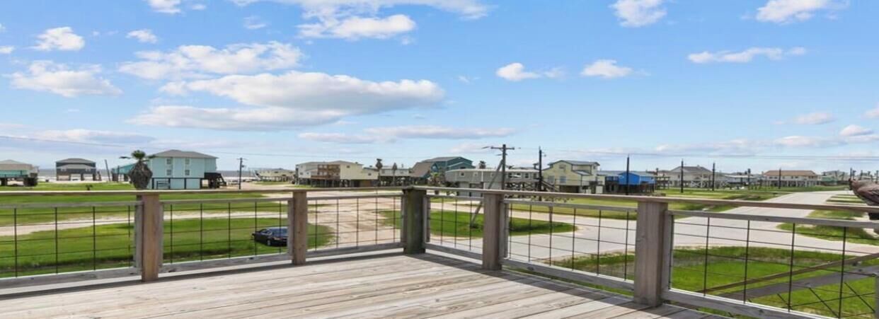 A wooden deck with a metal railing overlooking a parking lot and buildings.