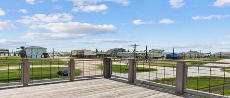 A wooden deck with a metal railing overlooking a parking lot and buildings.