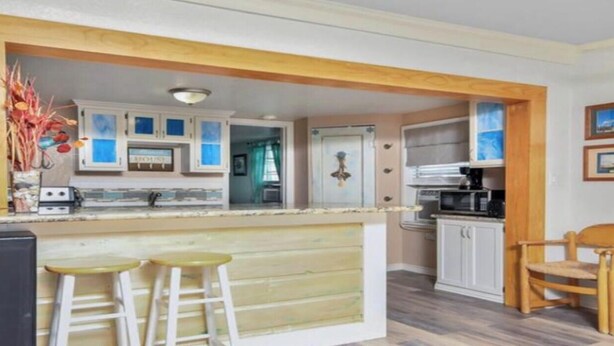 A kitchen with white cabinets, a microwave, and a coffee maker. There are two stools and a wooden chair.