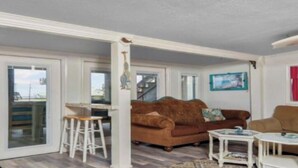 A living room with a brown sofa, a white coffee table, and a dining area with a white table and stools.
