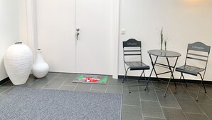 Ein Zimmer mit einer weißen Tür, zwei Stühle mit der Aufschrift 'Lieblingsplatz', einem kleinen Tisch und zwei weißen Vasen.