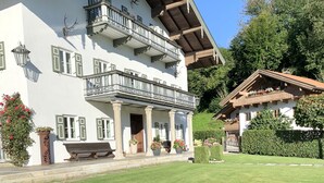 Ein zweistöckiges Gebäude mit Balkonen, einer Veranda und einem Garten.