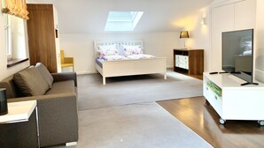 Ein modernes Schlafzimmer mit Oberlichter, einem Bett, einer Couch, einem Fernseher und einem Nachttisch.