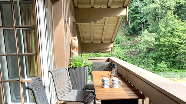 Ein Balkon mit Korbstühlen, einem Holztisch und zwei Tassen.