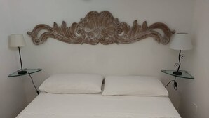 Un lit avec du linge de lit blanc, deux tables de chevet avec des lampes et une tête de lit décorative.