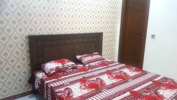 A bed with a floral-patterned bedspread and matching pillows, set against a patterned wallpaper and a wooden headboard.
