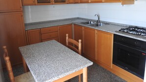 Une cuisine avec des meubles de rangement en bois, un plan de travail en granit, un évier, une cuisinière et une chaise.