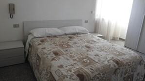 Une chambre d’hôtel avec un lit, une table de chevet, un téléphone et une fenêtre avec des rideaux.