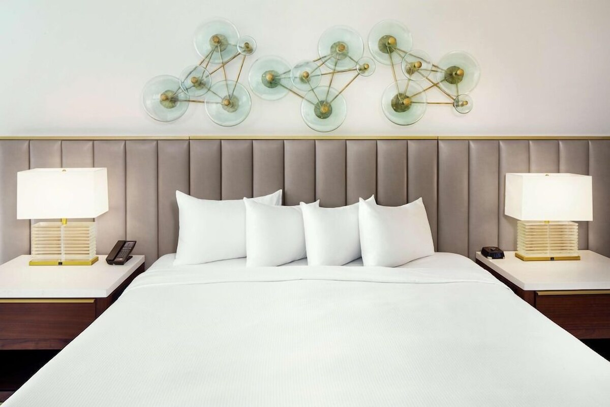 Camera d'albergo con un letto grande, due comodini con lampade e un'opera d'arte moderna sulla parete sopra il letto.